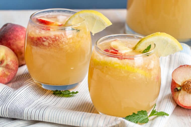 Delicious sparkling lemonade with peaches and lemons in two glass mugs. 