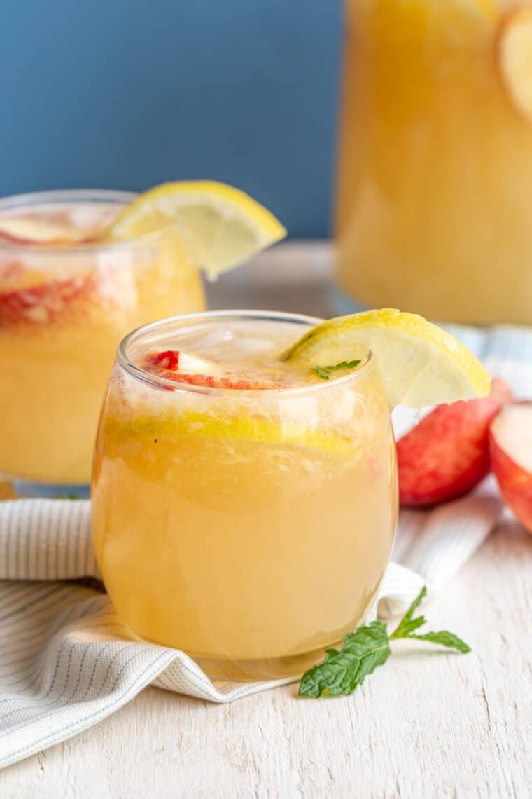 Fresh peach sparkling lemonade recipe in a cup with fresh peaches and lemons.