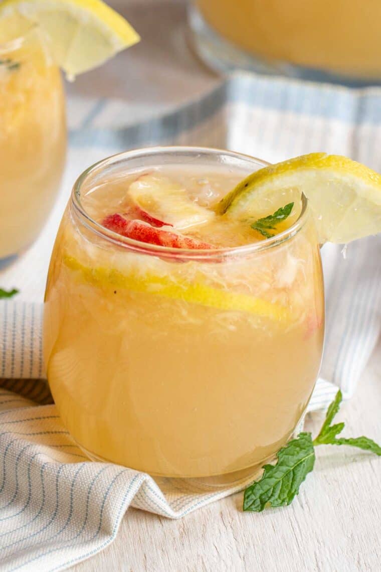 A glass full of sparkling peach lemonade topped with fresh peach slices and lemon slices.