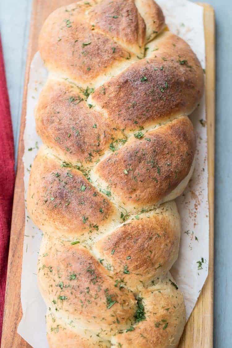 Soft bread braid with butter and herbs and a garlic crust on a cutting board.