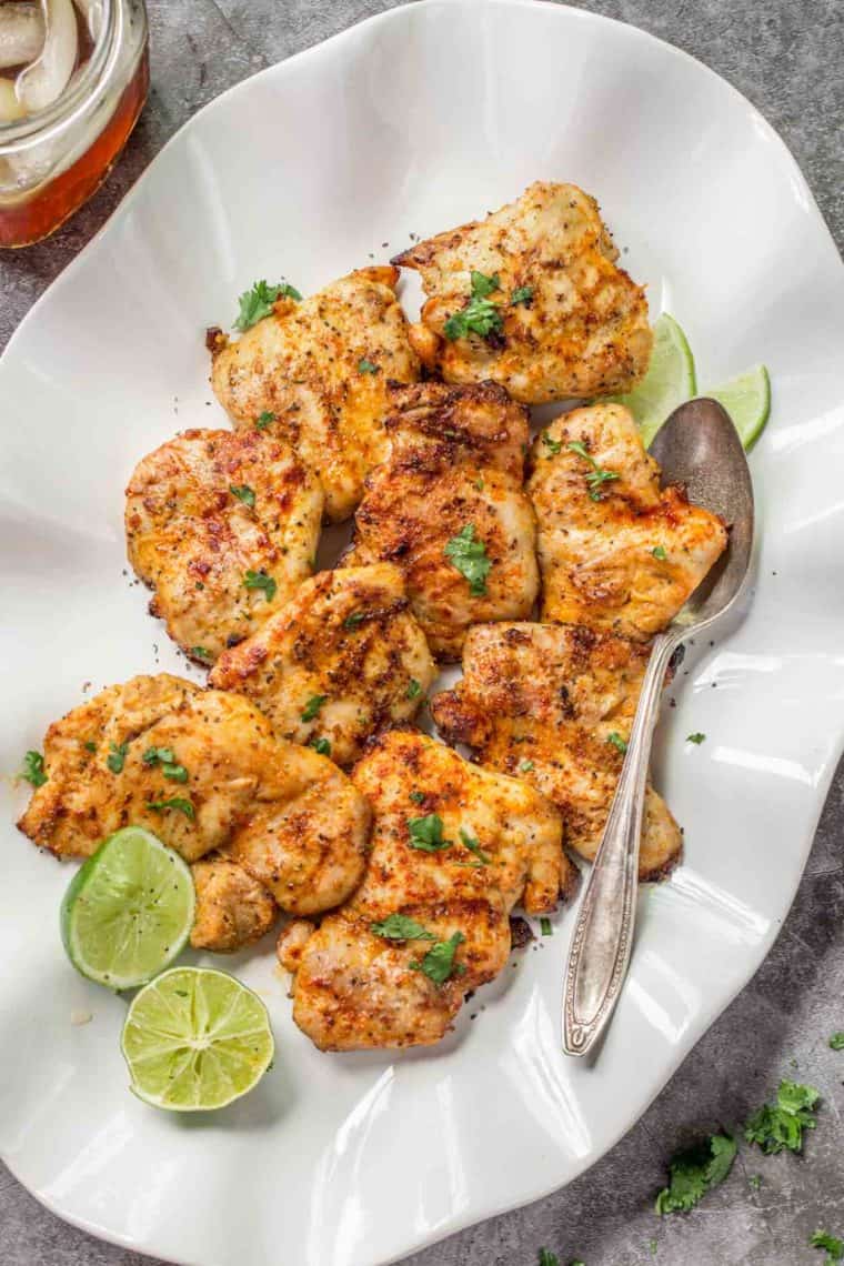 Tender grilled chicken thighs on a plate with lime and chopped cilantro.
