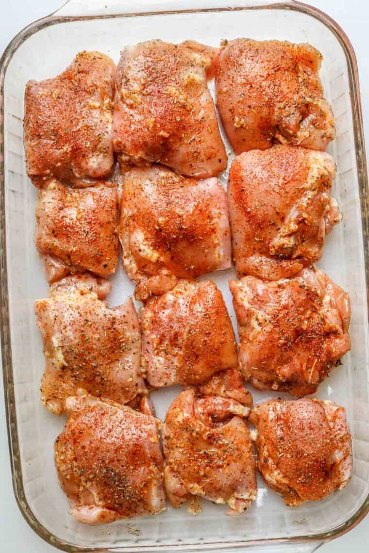 Seasoned boneless chicken thighs laid out in a baking dish ready to bake. 