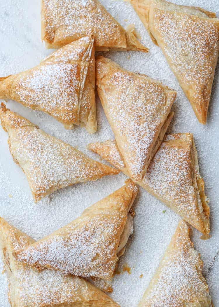 Pumpkin phyllo turnovers on a platter with powdered sugar and a icing drizzle.