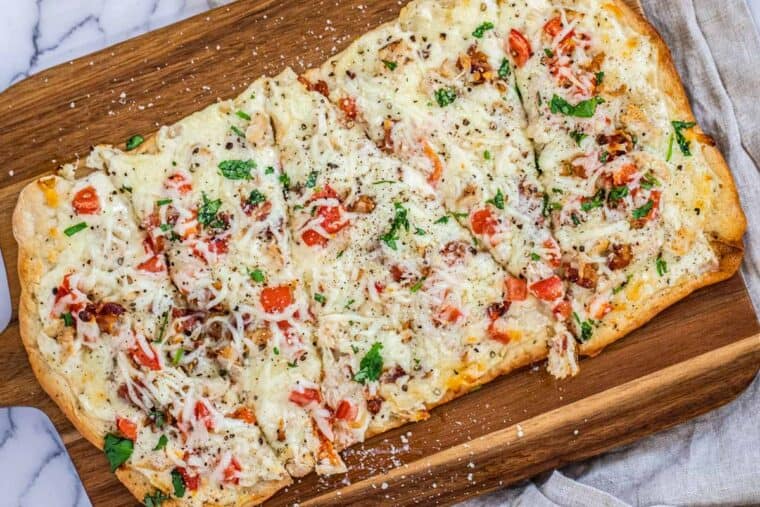 Sliced Alfredo chicken pizza topped with tomatoes and chopped cilantro. 