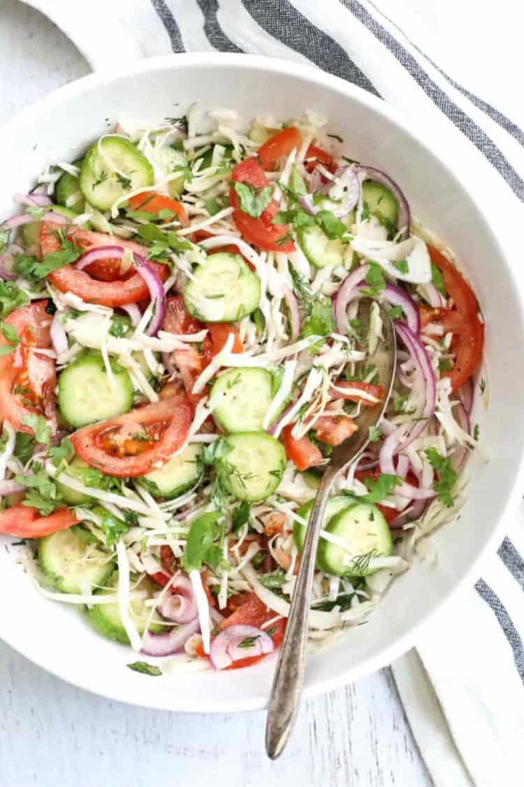 Cabbage cucumber tomato salad in a bowl with a spoon and towel.