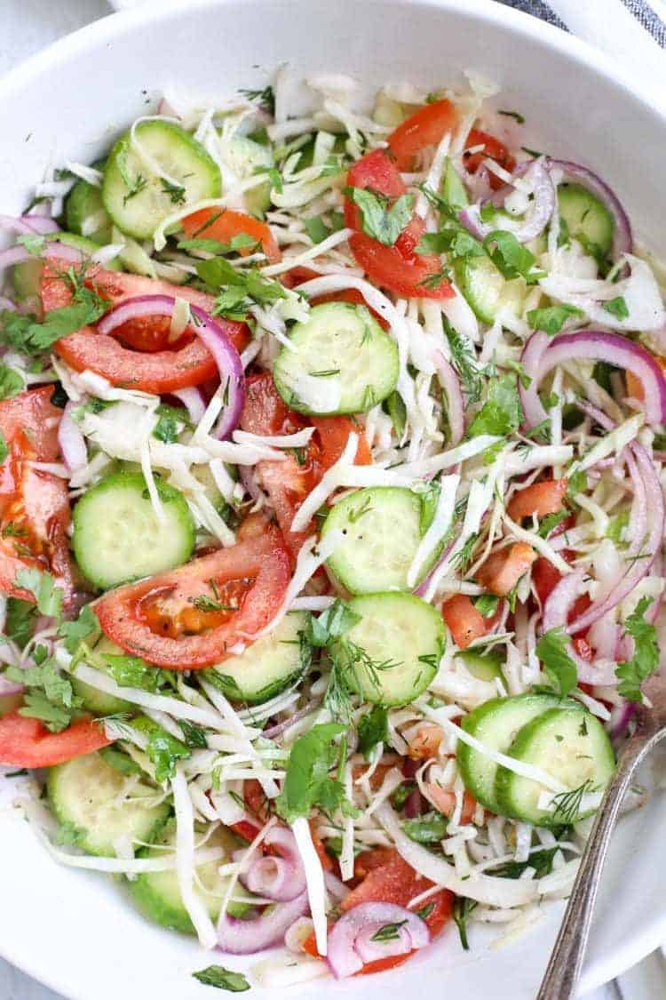 Close up of cabbage cucumber tomato salad in a large bowl with a spoon.
