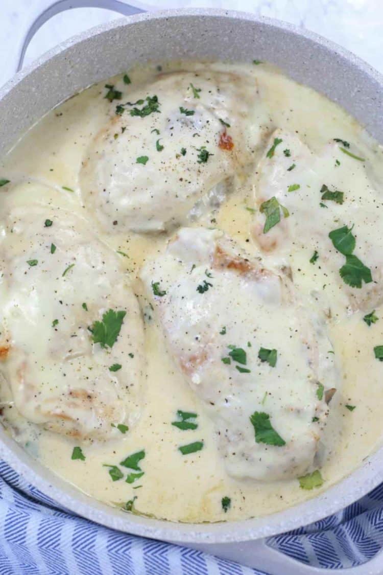 Mushroom stuffed chicken in Alfredo sauce in pan topped with fresh herbs.