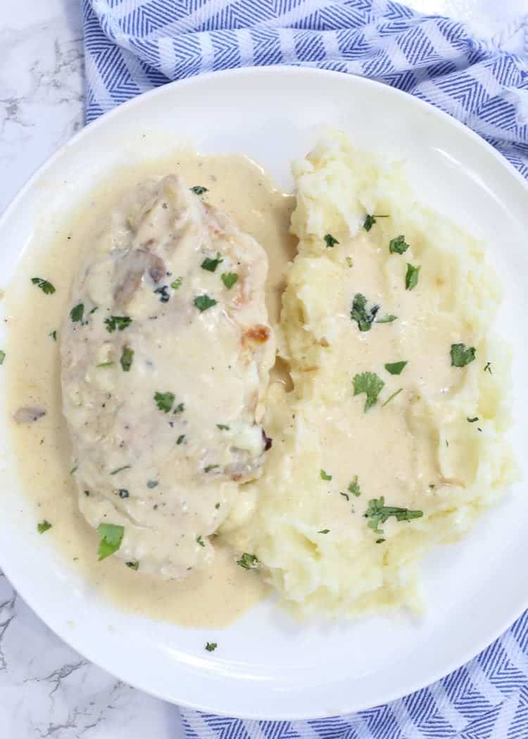 Mushroom stuffed chicken on a plate with mashed potatoes topped with fresh greens.