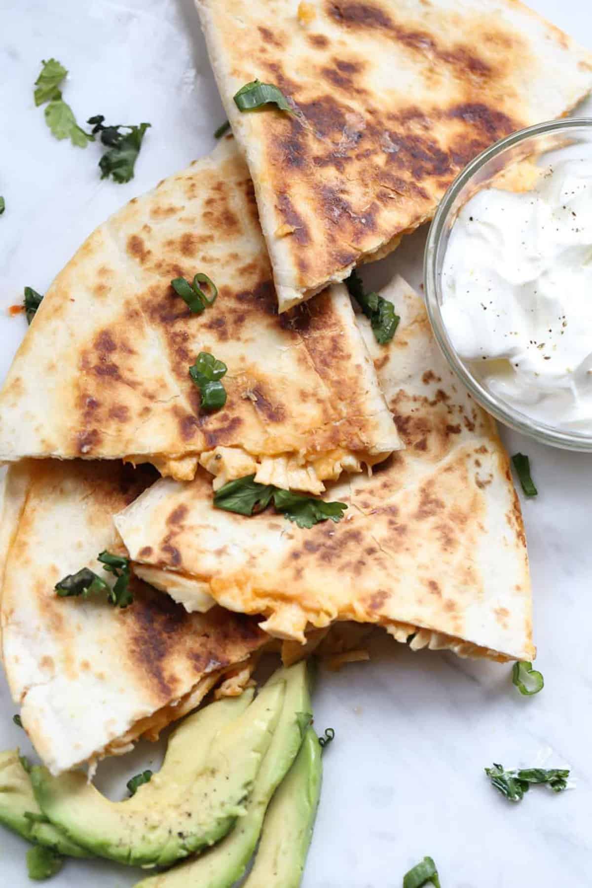 Chicken quesadillas on platter with sour cream and avocado.