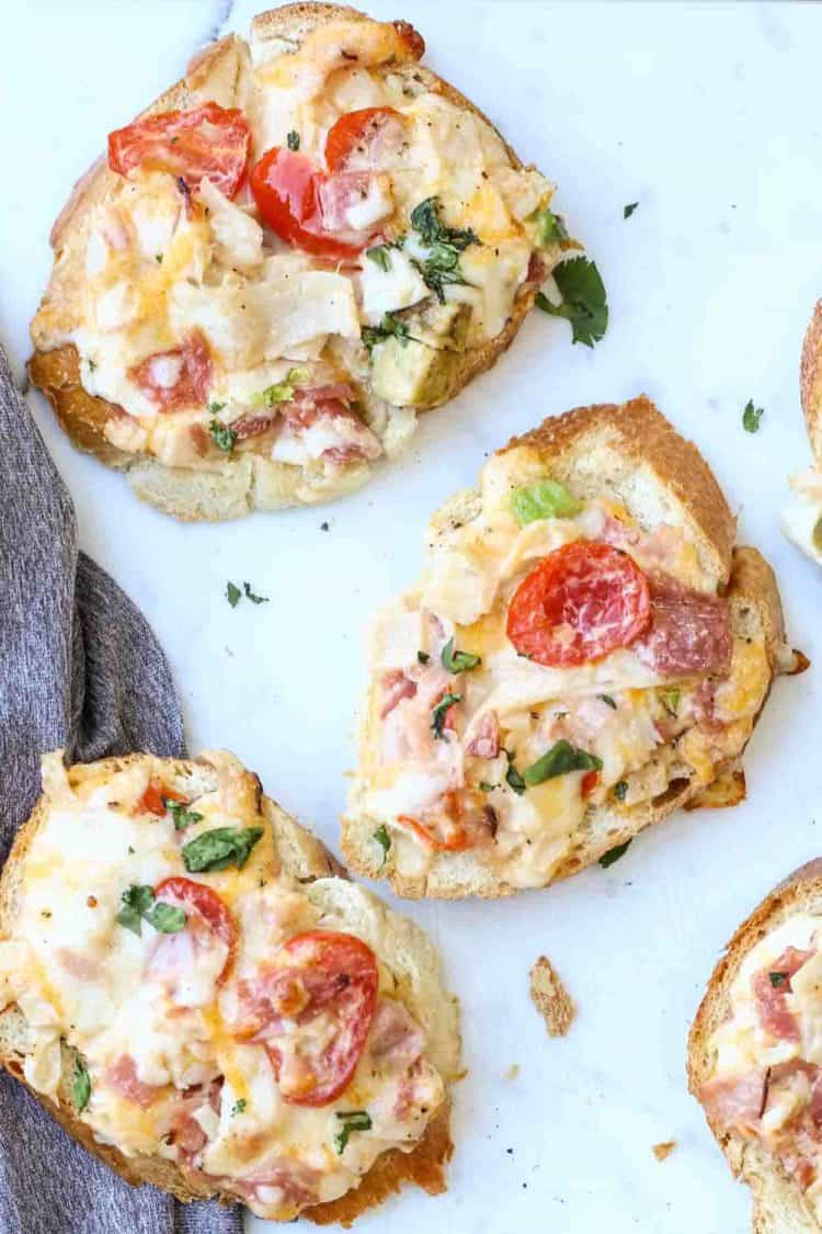 Simple canape sandwiches loaded with lunch meat, cheese and tomatoes on a platter.