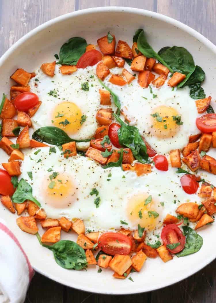 The sweet potatoes with spinach, tomatoes, and eggs in a skillet with fresh greens.