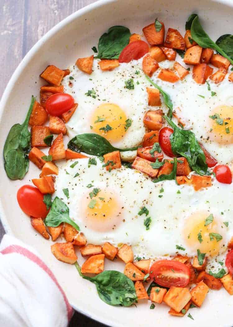Egg and sweet potato breakfast in a skillet with spinach and fresh greens. 