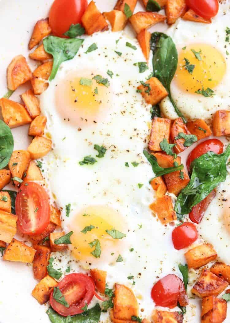 Sweet potato breakfast with cooked eggs, spinach, and tomatoes topped with greens and pepper.