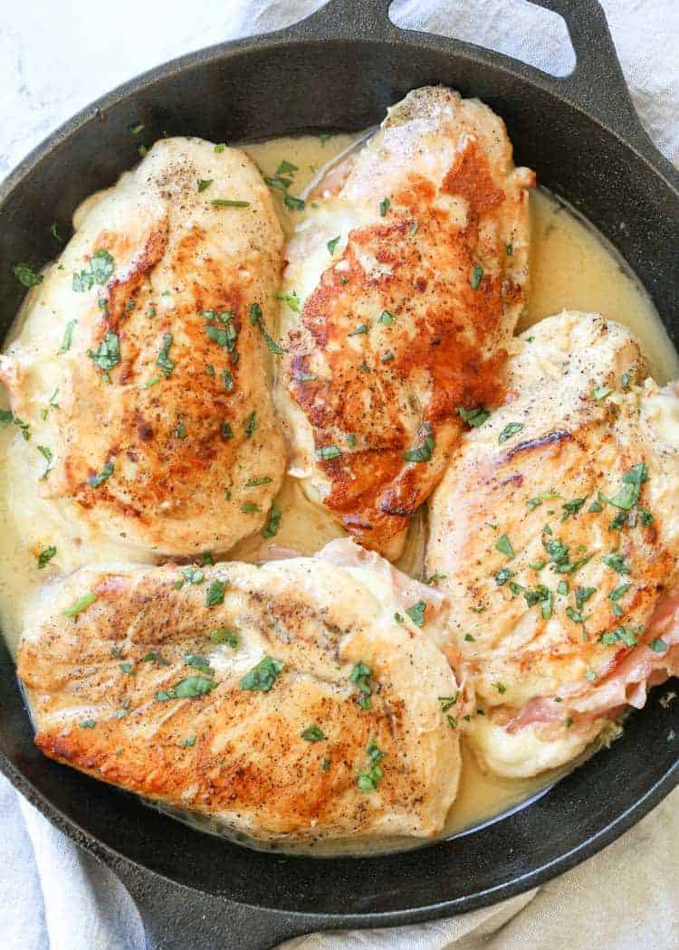 Chicken breasts in a skillet with lemon sauce, stuffed with ham and cheese in a skillet.