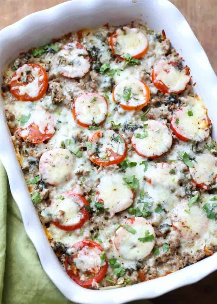 Easy meat and potato casserole recipe with fresh herbs in a white casserole dish next to a green rag.