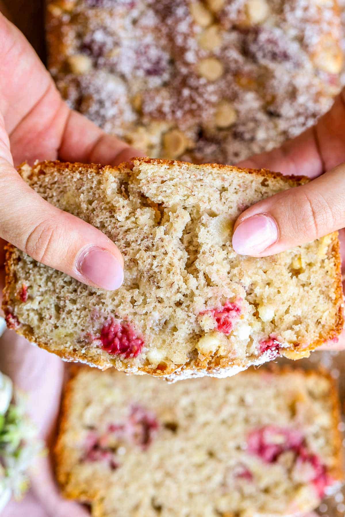 A slice of banana bread with raspberries being ripped in half. 