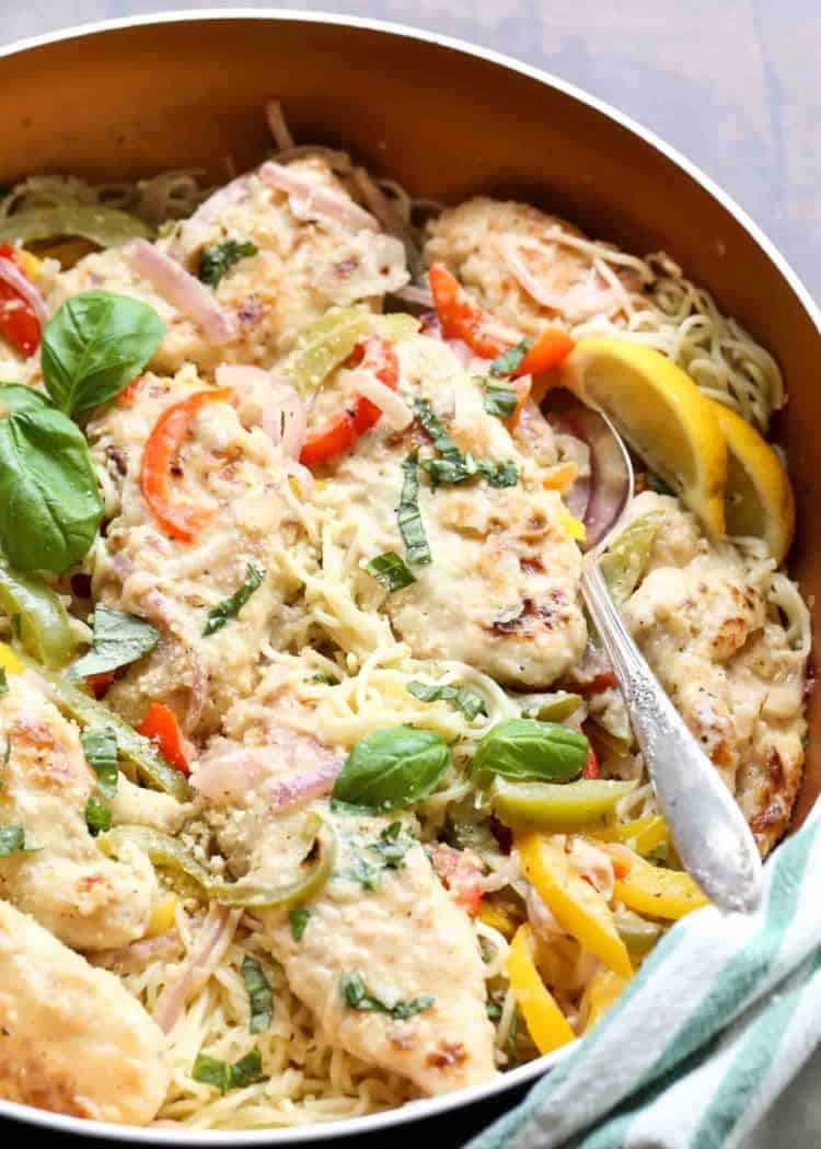Angel hair pasta in a skillet with chicken and vegetable garnished with fresh lemons.