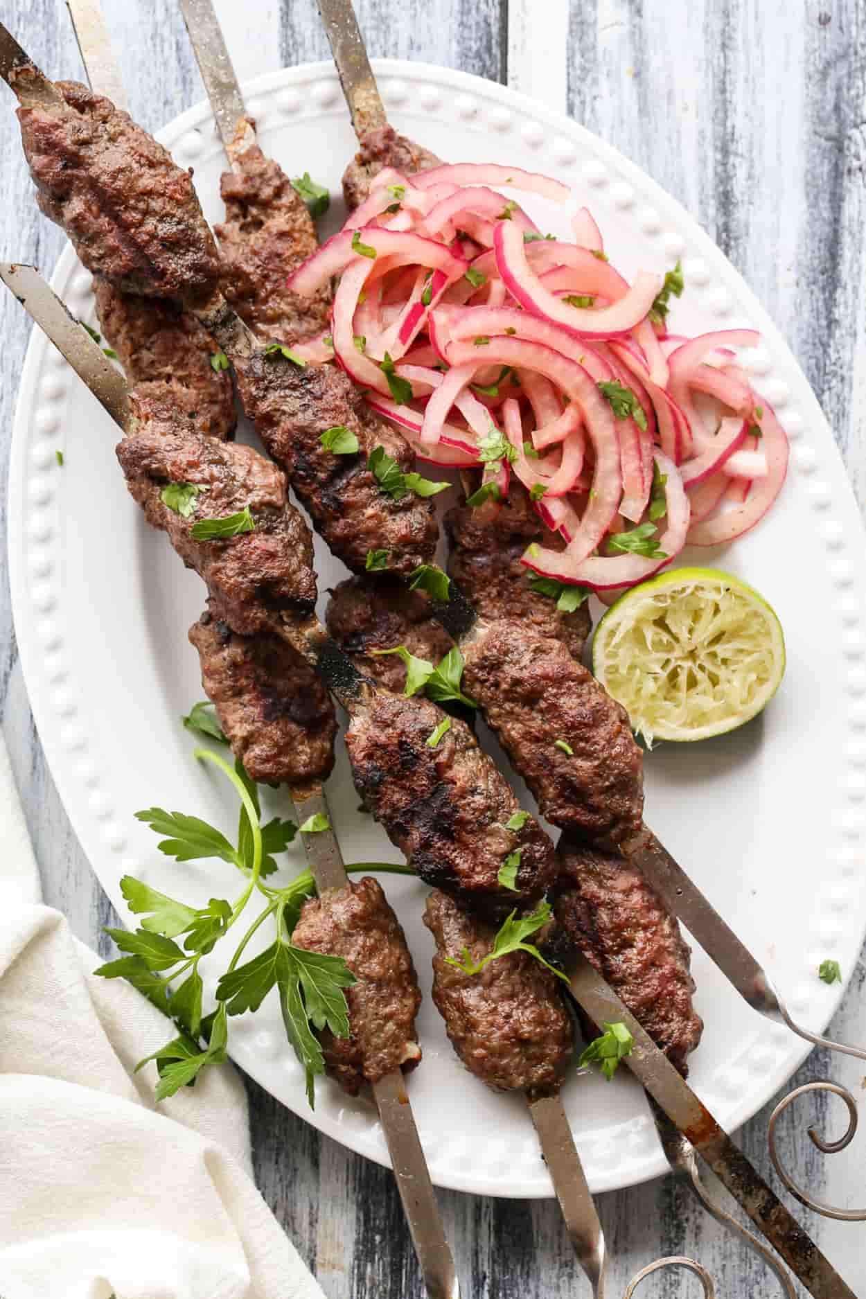 Ground beef kabobs on skewers in a plate with onion salad.