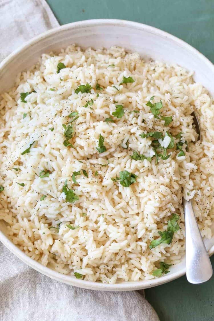White rice in a bowl with a spoon and cilantro on top.