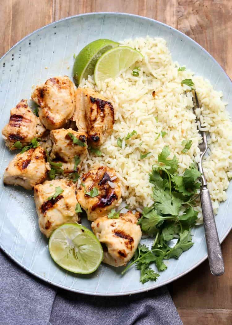 Juicy grilled chicken kebabs with a side of rice in a plate with a fork and limes.