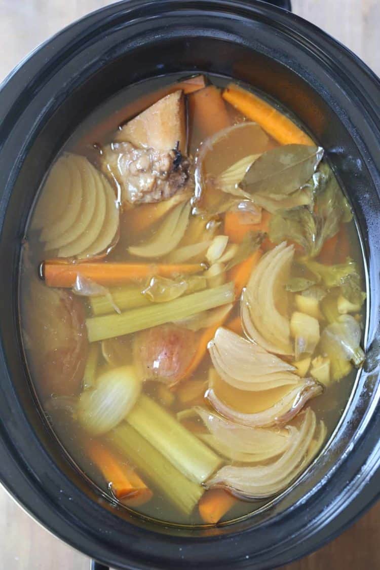 Bone Broth in a crock pot with bones, onions, celery, and carrots.