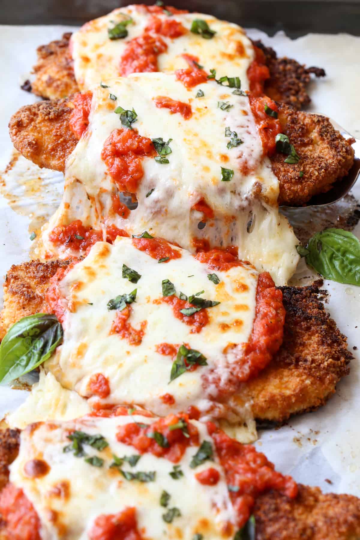 Crispy parmesan chicken with marinara and topped with cheese on a baking sheet.