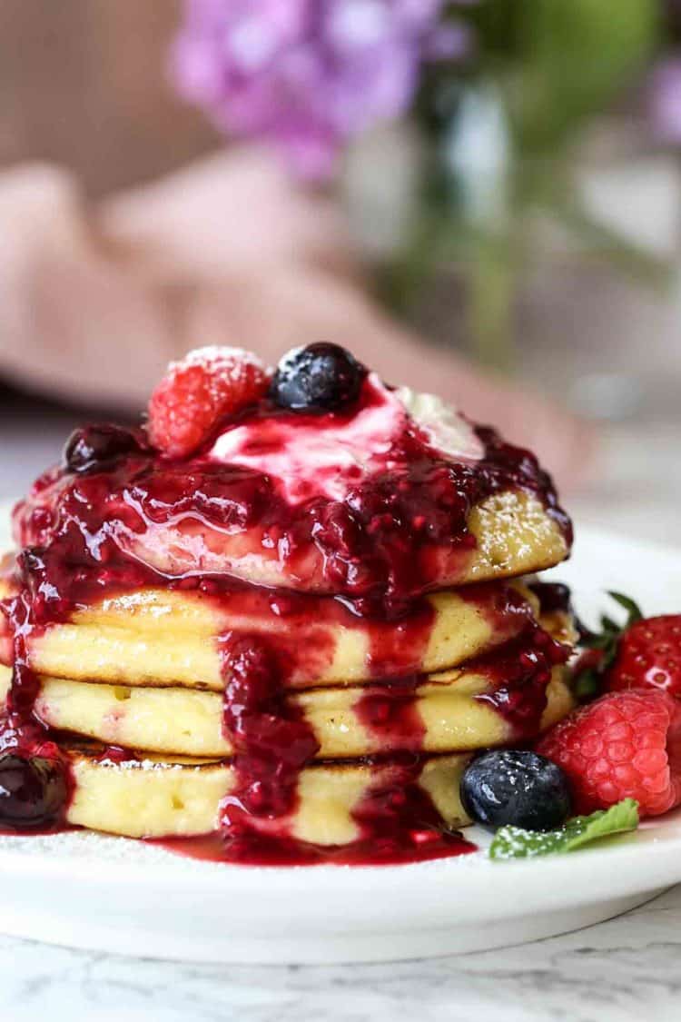 Stacked pancakes topped with berry syrup on a plate.