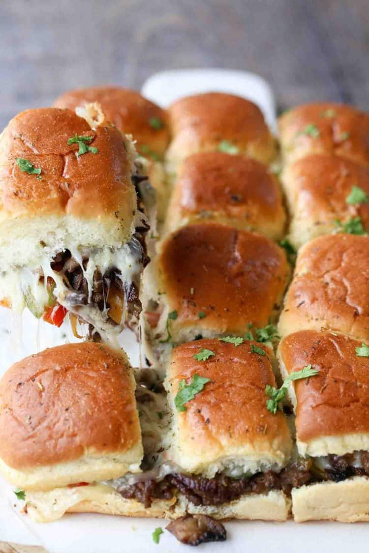 Philly cheese steak sliders on a board with cilantro on top, with on slider picked up.