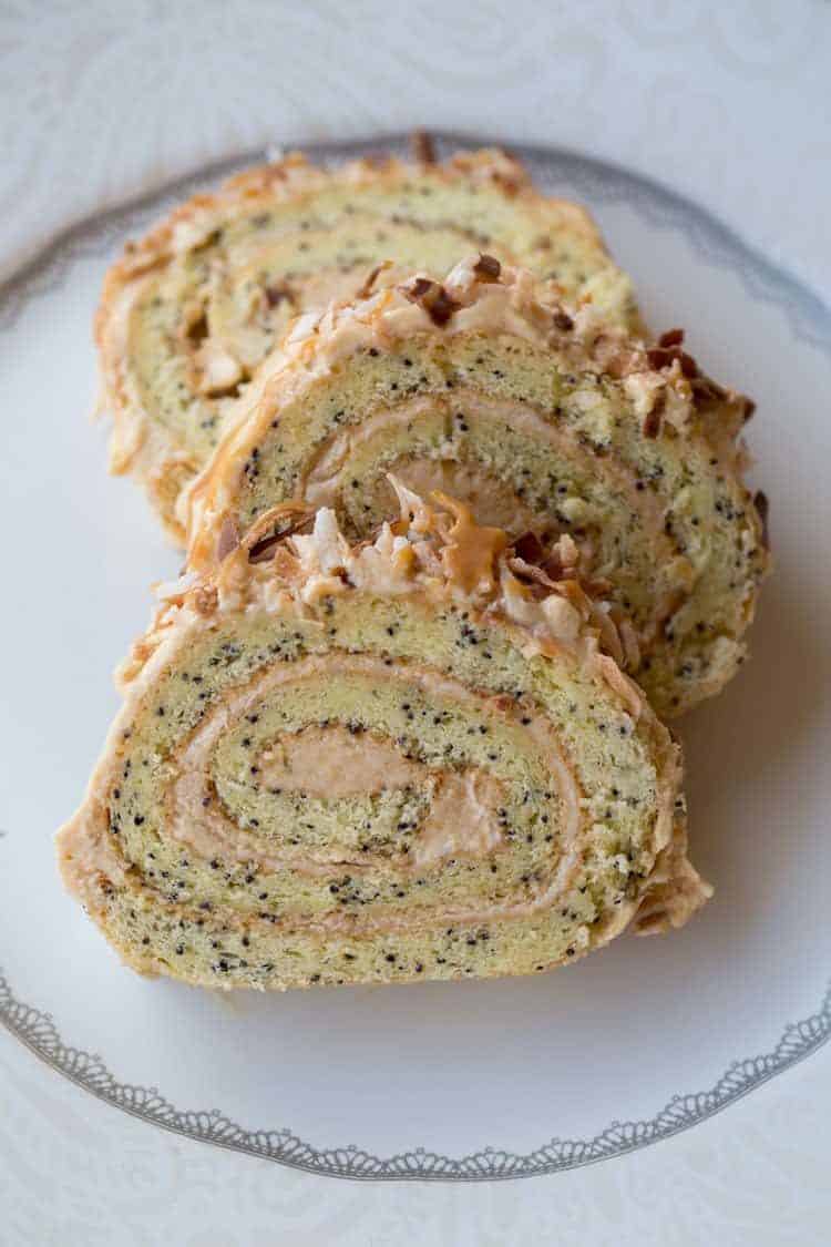 Three slices of Poppy Seed Roulade on a plate topped with toasted coconut and chocolate shavings.