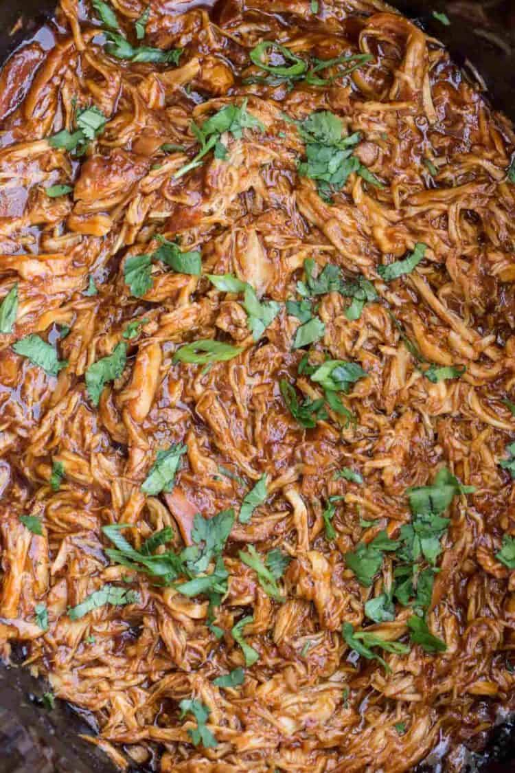 BBQ pulled chicken crock pot recipe topped with fresh greens in a slow cooker.