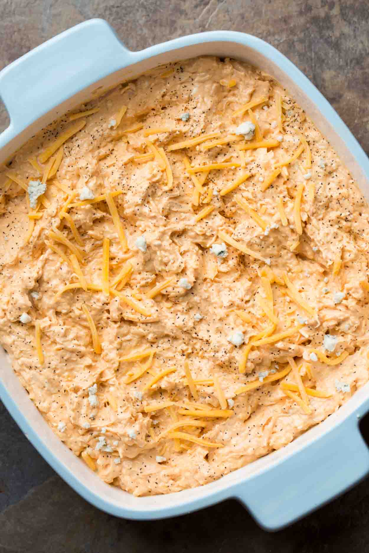 A casserole dish with the mixed buffalo dip ingredients. 