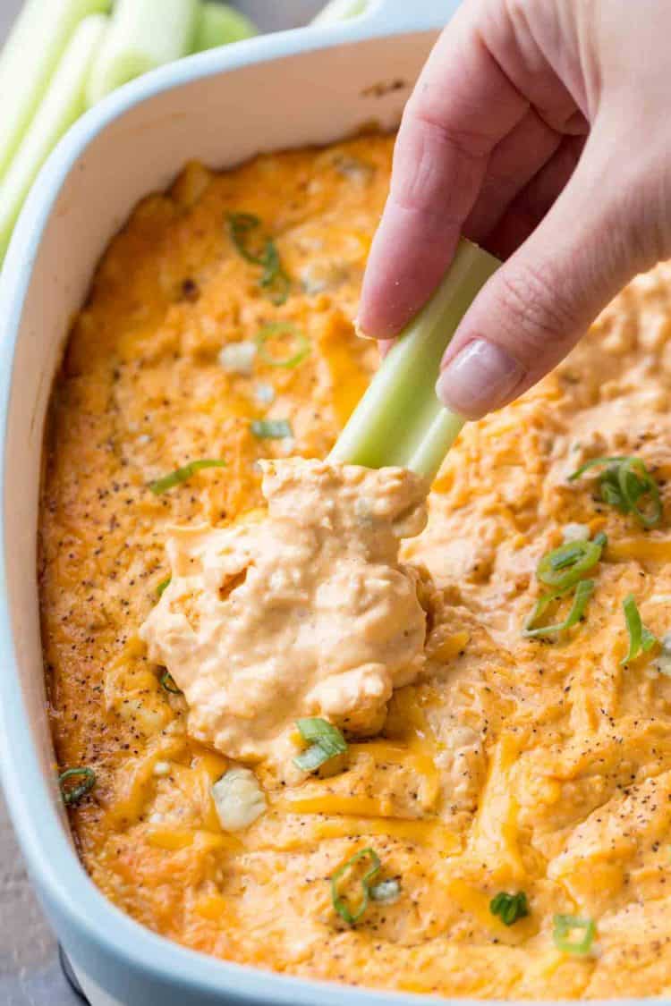 Buffalo chicken dip with a celery stick and chopped fresh greens in a casserole dish.