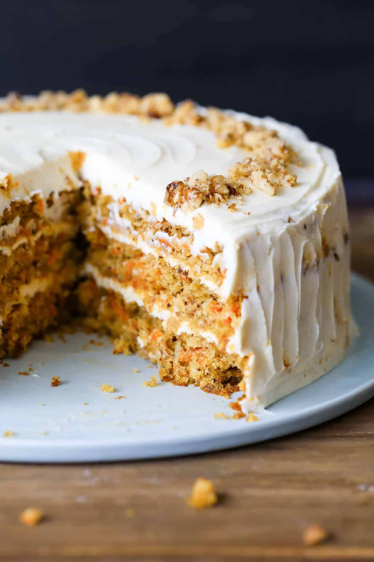 The best carrot cake on a cake platter with a cream cheese frosting topped with walnuts.
