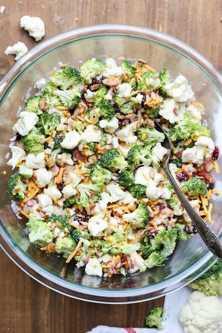 Cauliflower broccoli recipe salad with a homemade dressing in a mixing bowl with a spoon.