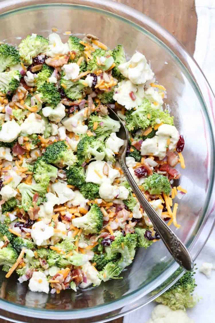 Cauliflower broccoli salad recipe with cheese, bacon, craisins, and sunflower seeds in a bowl with a spoon.