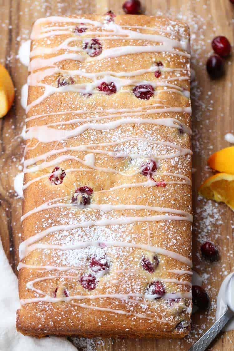 Sweet cranberry bread loaf cut into slices, topped with a sugar glaze and powdered sugar.