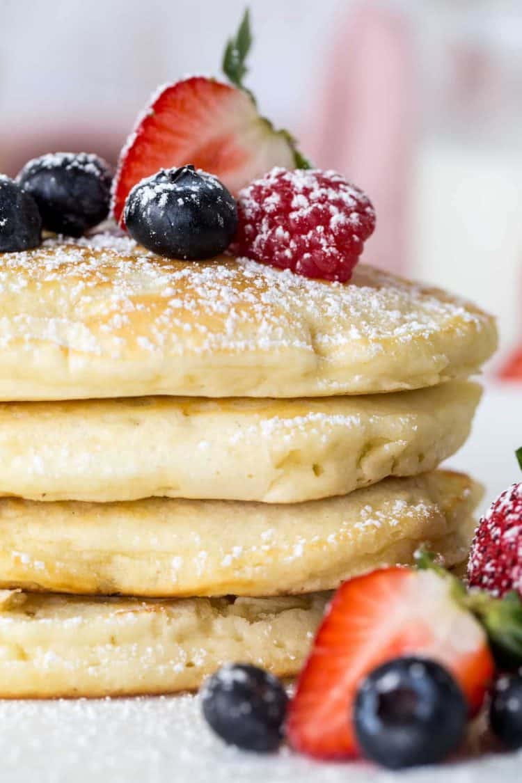 Homemade pancakes stacked on top of each other with berries and sprinkled with powdered sugar.