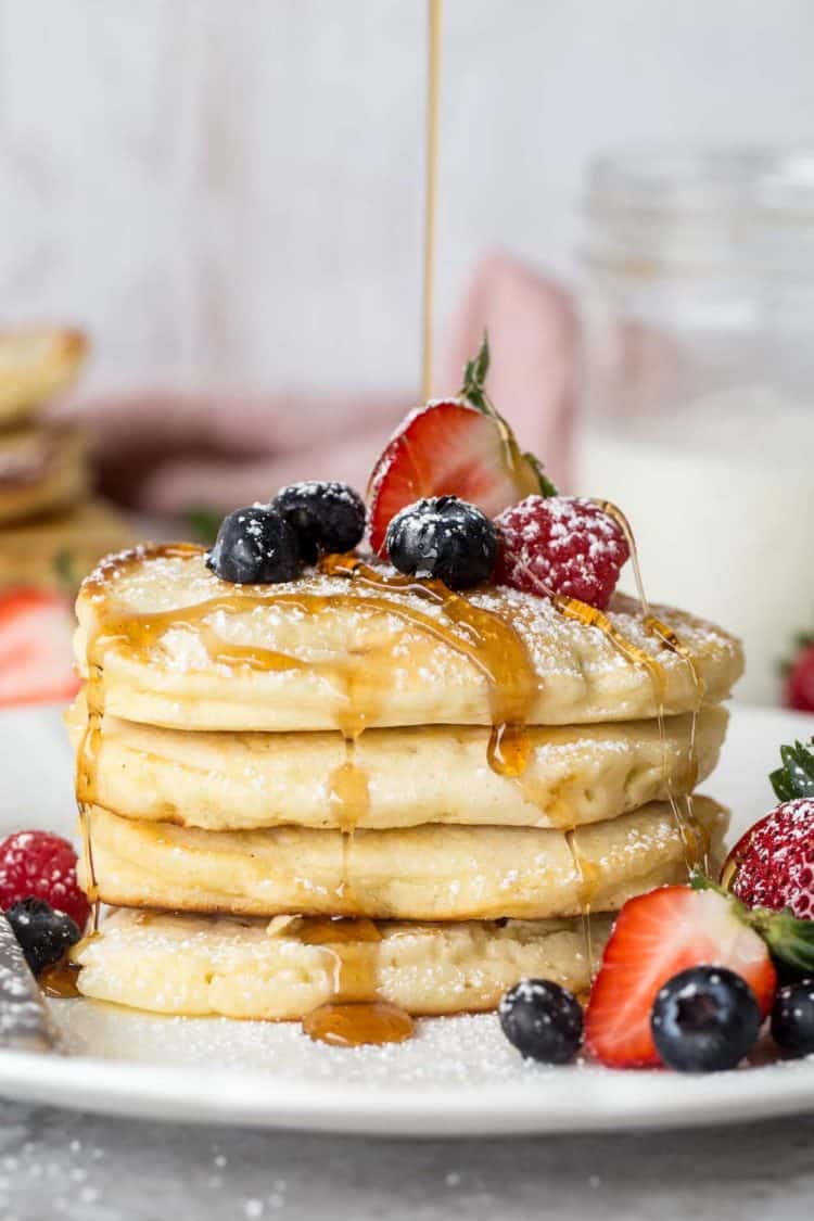 Easy pancake recipe made with butter and milk, syrup being poured in a stack of pancakes with berries.