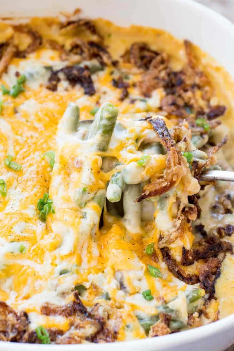 Green bean casserole recipe topped with cheese, onion rings, and chopped greens.