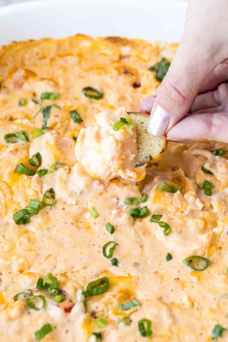 Buffalo shrimp dip in a casserole dish with a bagel chip and fresh greens.