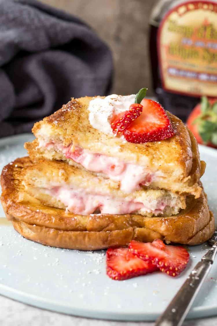Stuffed french toast on a blue plate cut in half and topped with strawberries. 
