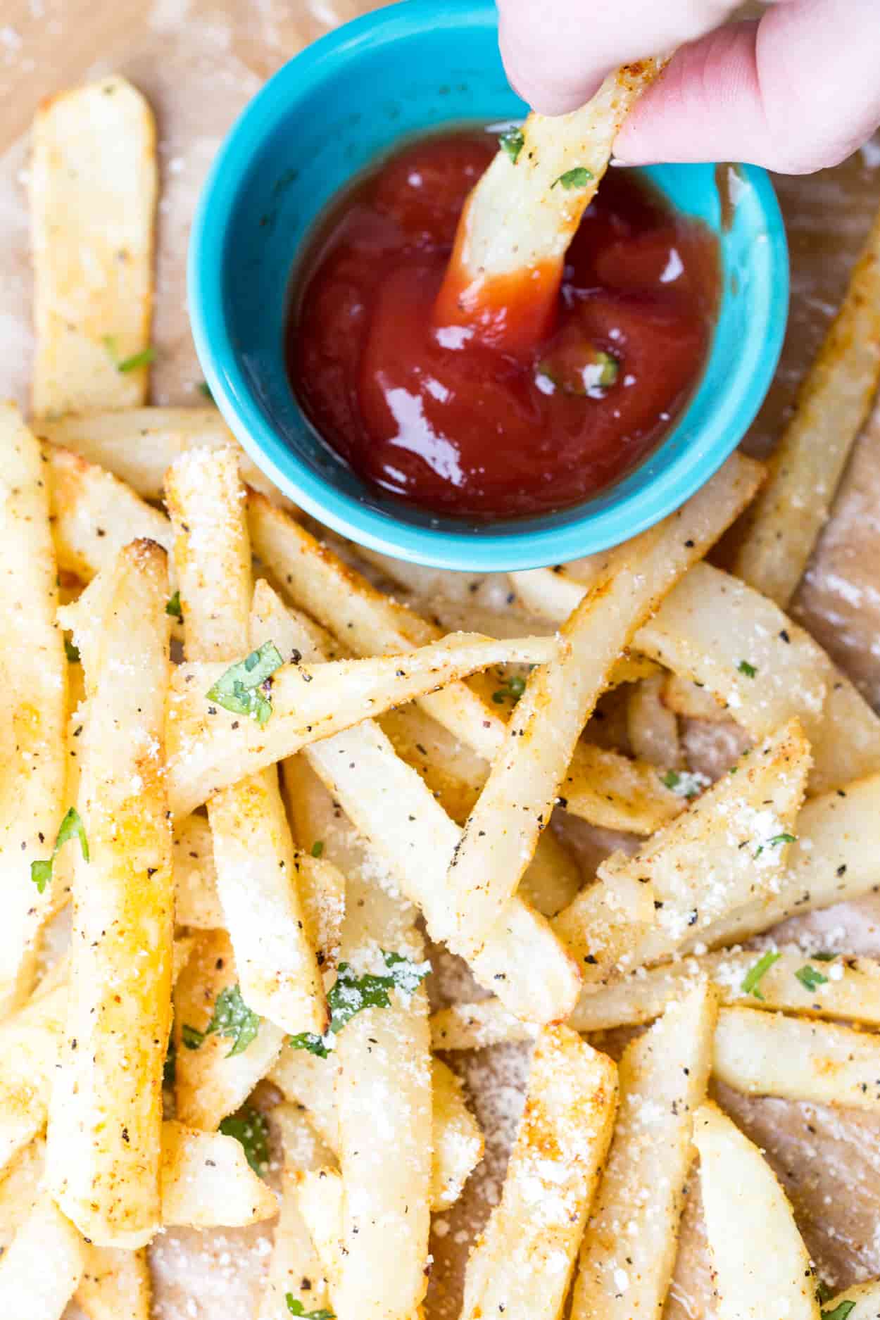 French fries topped with greens and parmesan cheese, dipped into ketchup.