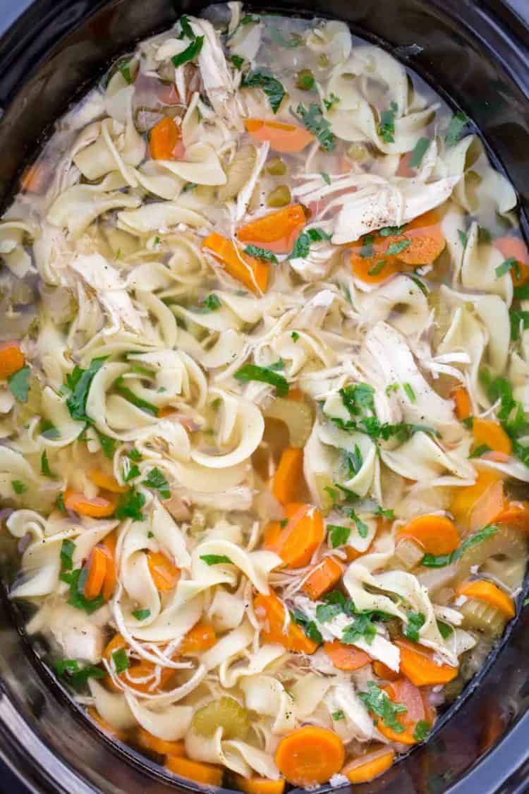 Crockpot Chicken noodle soup recipe in a crock pot topped with fresh greens.