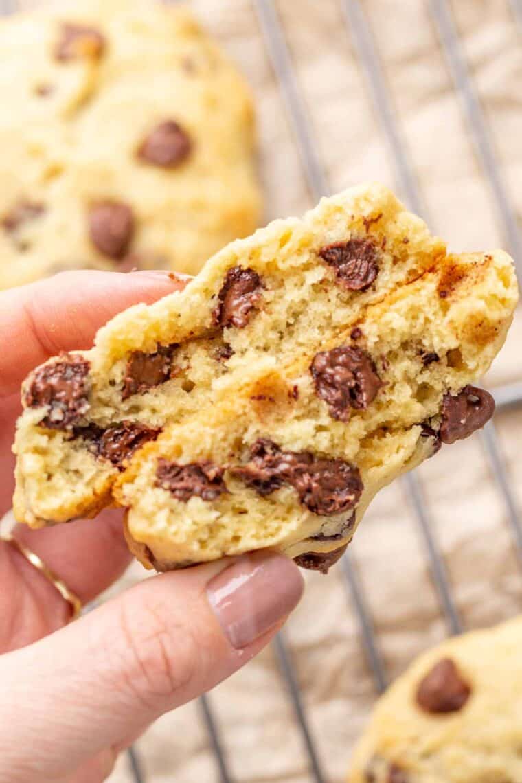 Chocolate chip cookie cut in half being held showing the inside. 