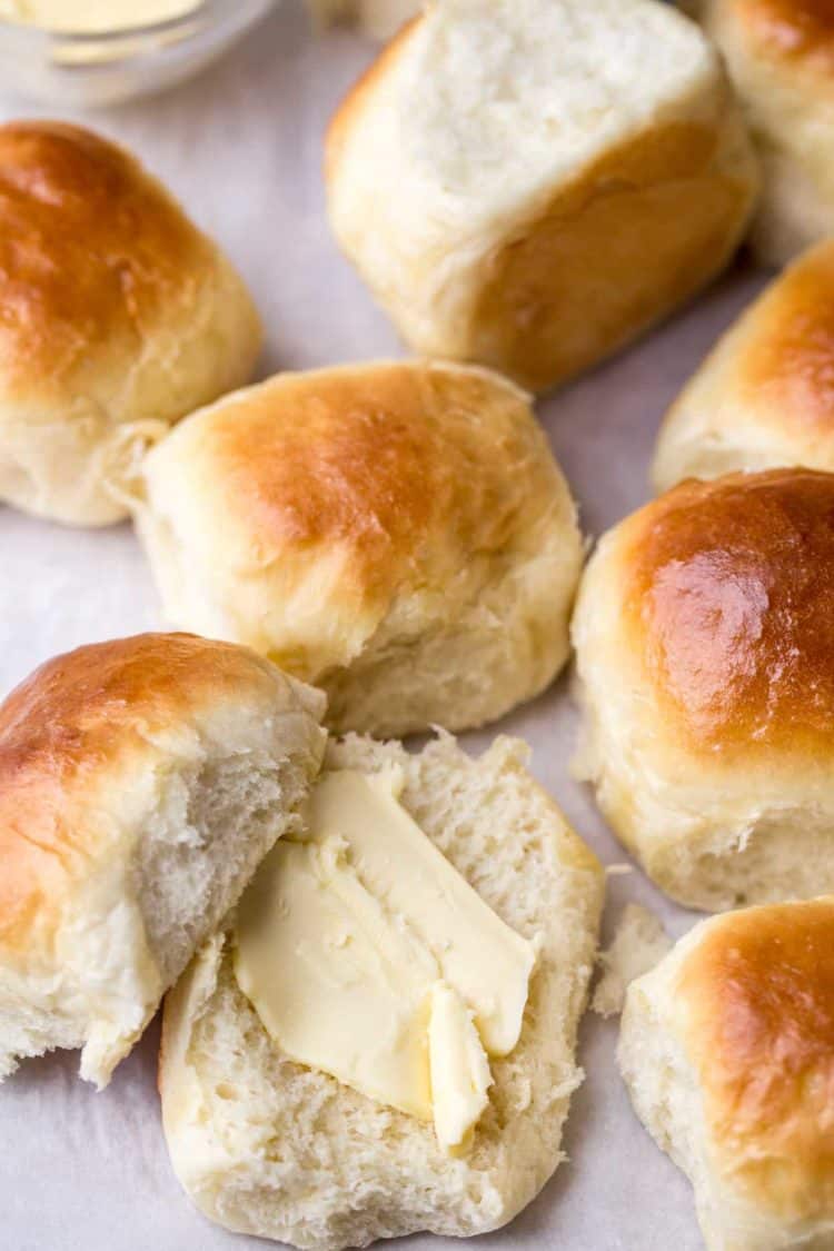 Soft and fluffy dinner rolls laid out next to a dinner roll cut in half with butter. 