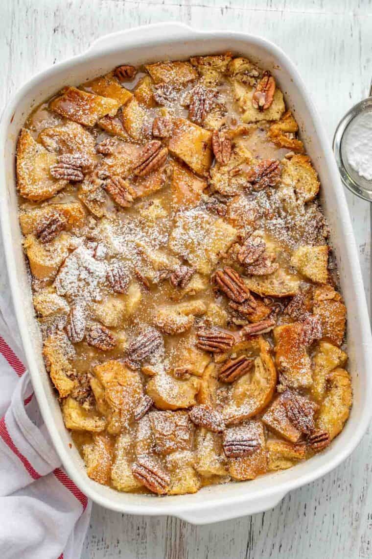 French toast casserole in a white casserole dish topped with powdered sugar. 