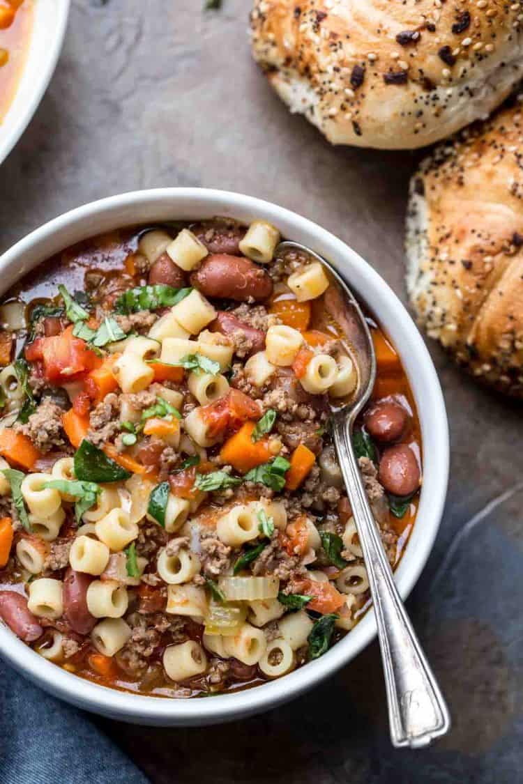 Pasta fagioli in a bowl with a spoon and bread on the side.