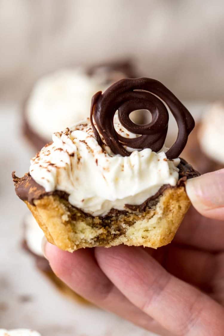 Tiramisu tartlet bitten into, lightly dusted with cocoa powder. Topped with a chocolate swirl.