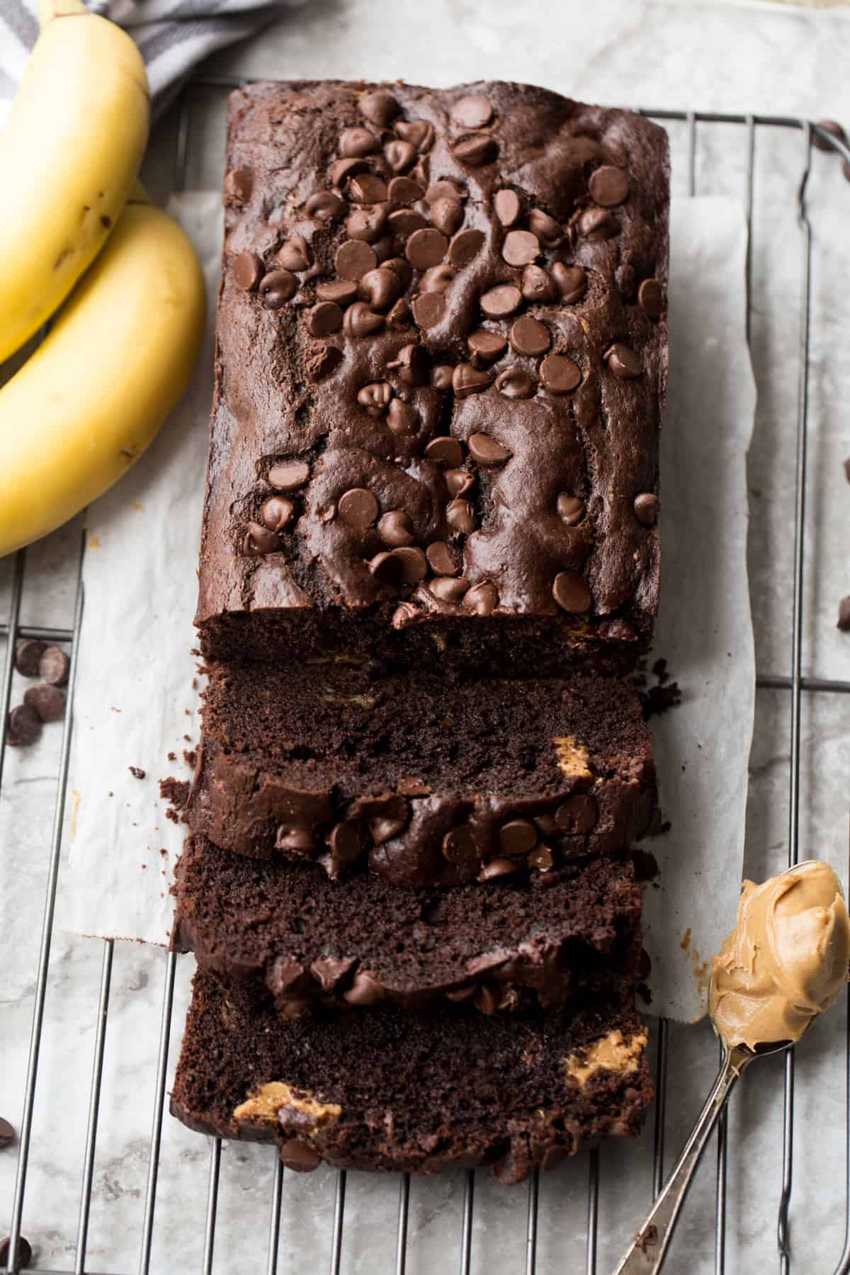 Peanut butter chocolate banana bread load cut into slices. Next to bananas and a spoon of peanut butter.