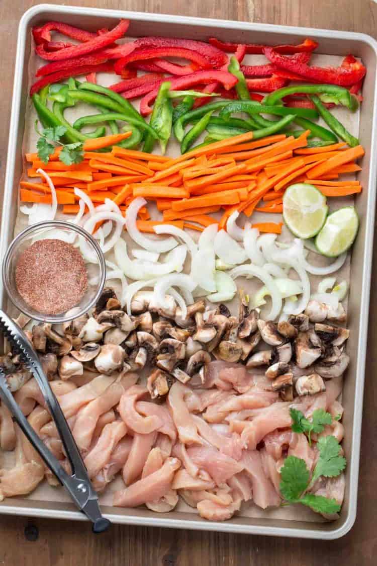 Cut chicken strips, peppers, carrots, mushrooms, and onions on a with seasoning on a baking dish.